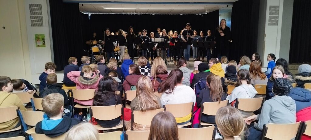 Schüler sitzen im Publikum, während eine Band auf der Bühne spielt.