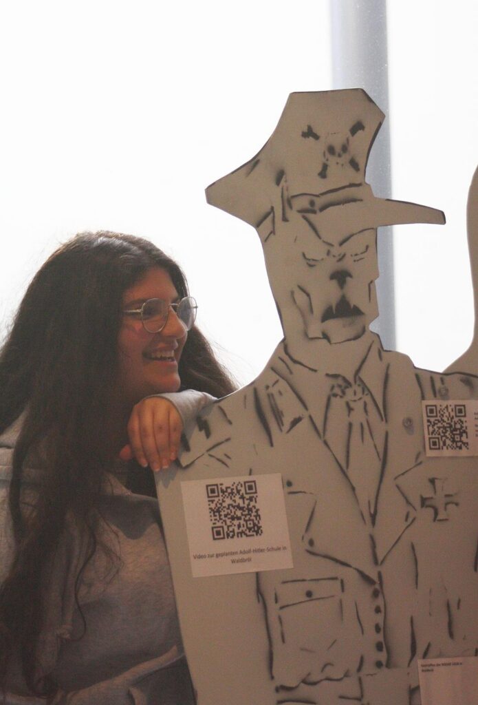 Eine Person steht neben einer Pappfigur eines Polizisten mit QR-Codes.