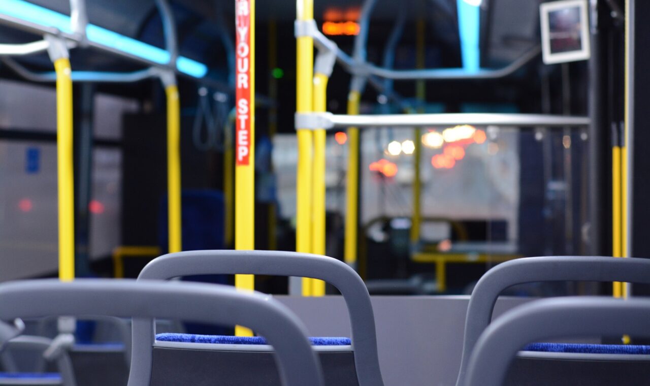 Innenansicht eines leeren Busses mit blauen Sitzen und gelben Haltestangen.