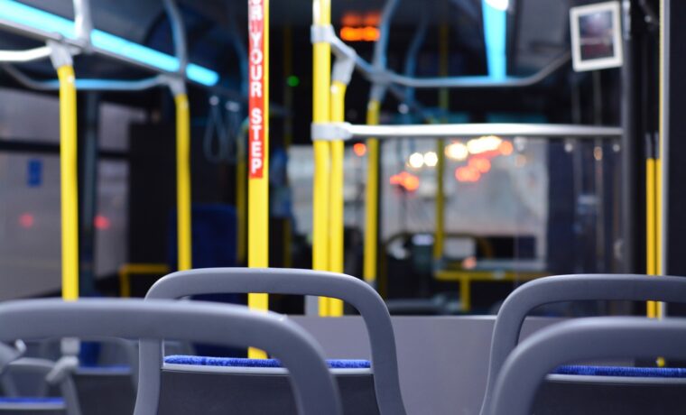Innenansicht eines leeren Busses mit blauen Sitzen und gelben Haltestangen.