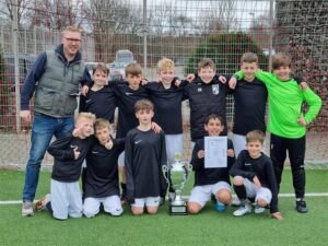 Schulfußballmannschaft mit Pokal und Urkunde, Gruppenfoto auf dem Spielfeld.
