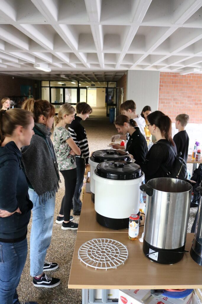 Leute stehen an einem Tisch mit Getränken und Snacks in einer Schulumgebung.