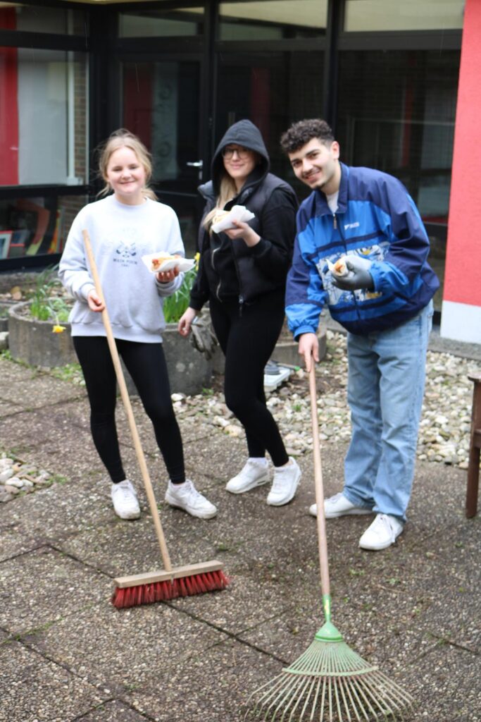 Drei Schüler fegen gemeinsam im Schulgarten.