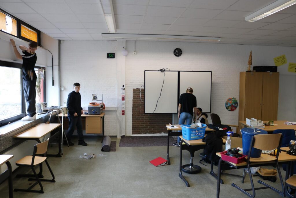 Schüler arbeiten im Klassenzimmer an Fenstern und Tischen.