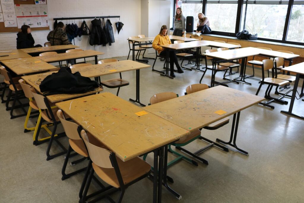 Leerer Klassenraum mit Tischen und Stühlen, eine Person sitzt am Fenster.