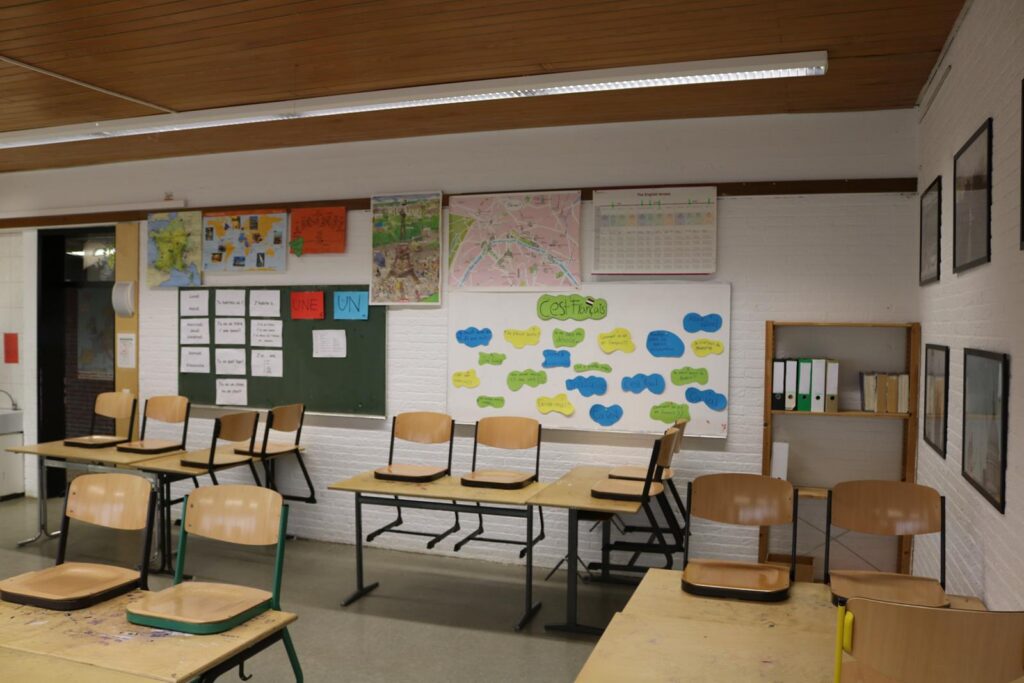 Klassenzimmer mit Tischen, Stühlen und zahlreichen Wandpostern.