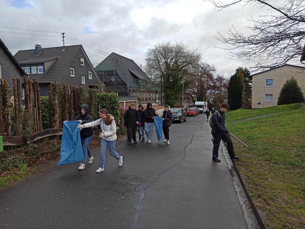 Gruppe von Schülern mit blauen Planen geht eine Straße entlang.