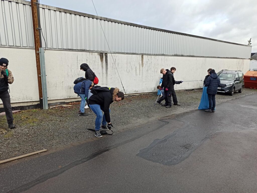 Menschen sammeln Müll in einer Straße neben einer Lagerhalle.