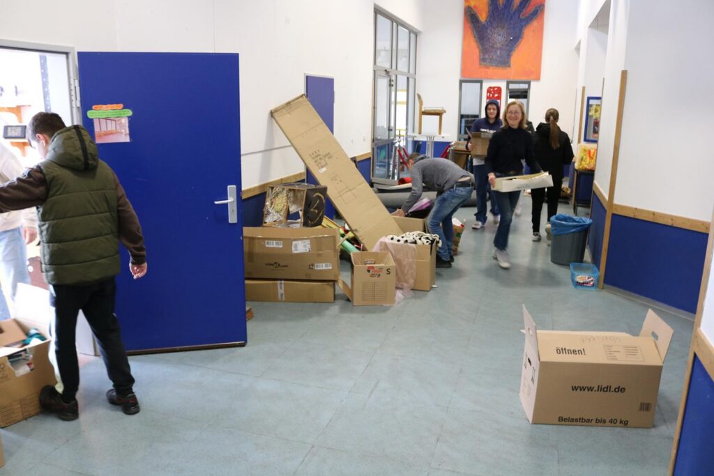 Schüler bringen Kartons und Materialien in einen Flur mit blauen Wänden.