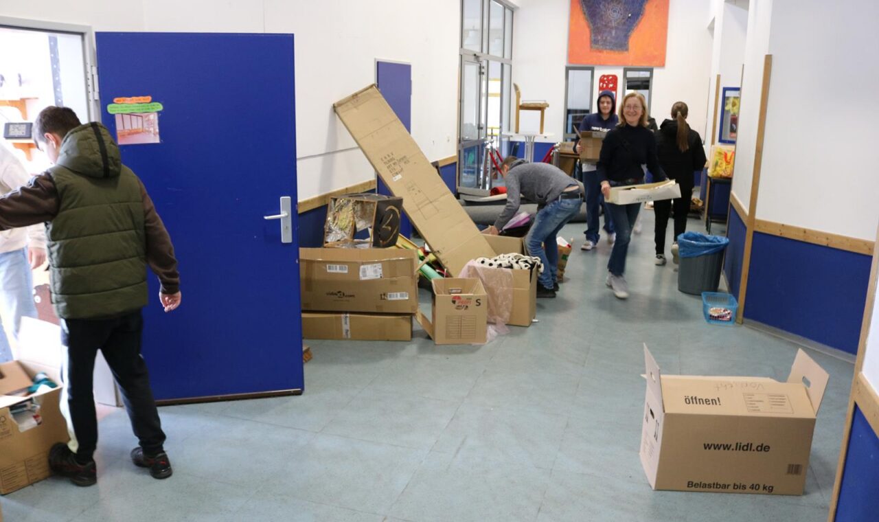 Schüler bringen Kartons und Materialien in einen Flur mit blauen Wänden.