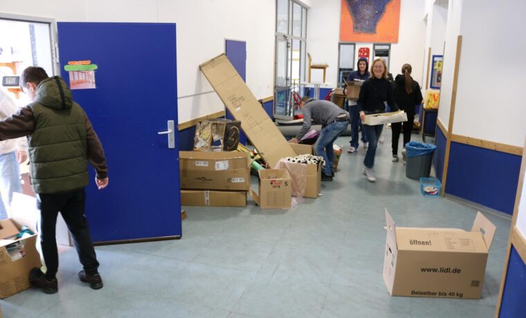 Schüler bringen Kartons und Materialien in einen Flur mit blauen Wänden.