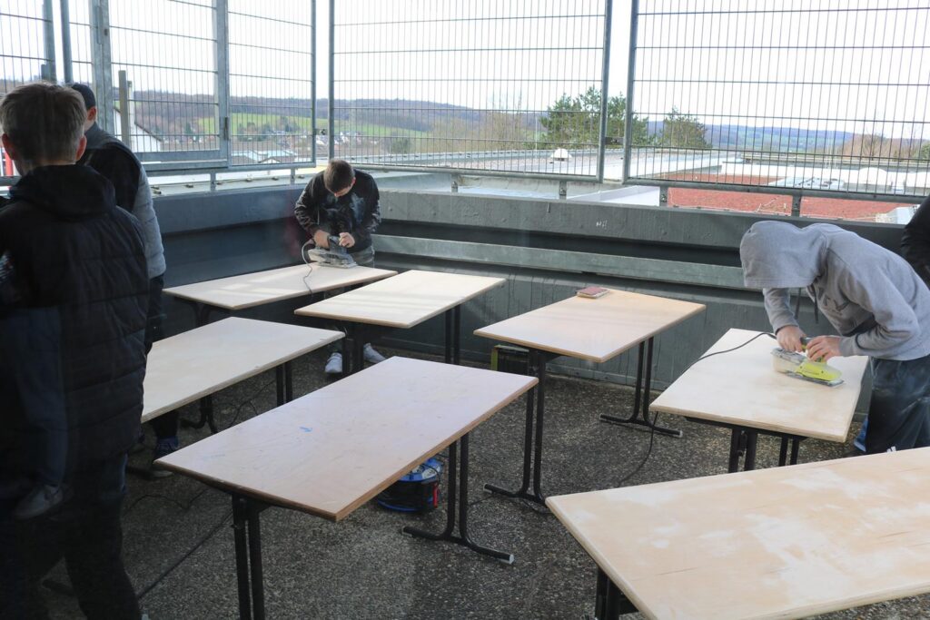 Schüler arbeiten an Tischen im Freien und bearbeiten Holz.