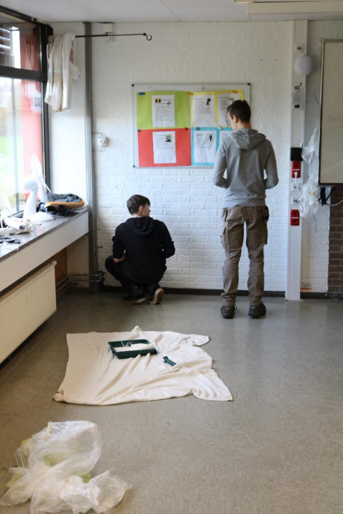 Zwei Schüler arbeiten an einer Wand, einer sitzt und der andere steht.