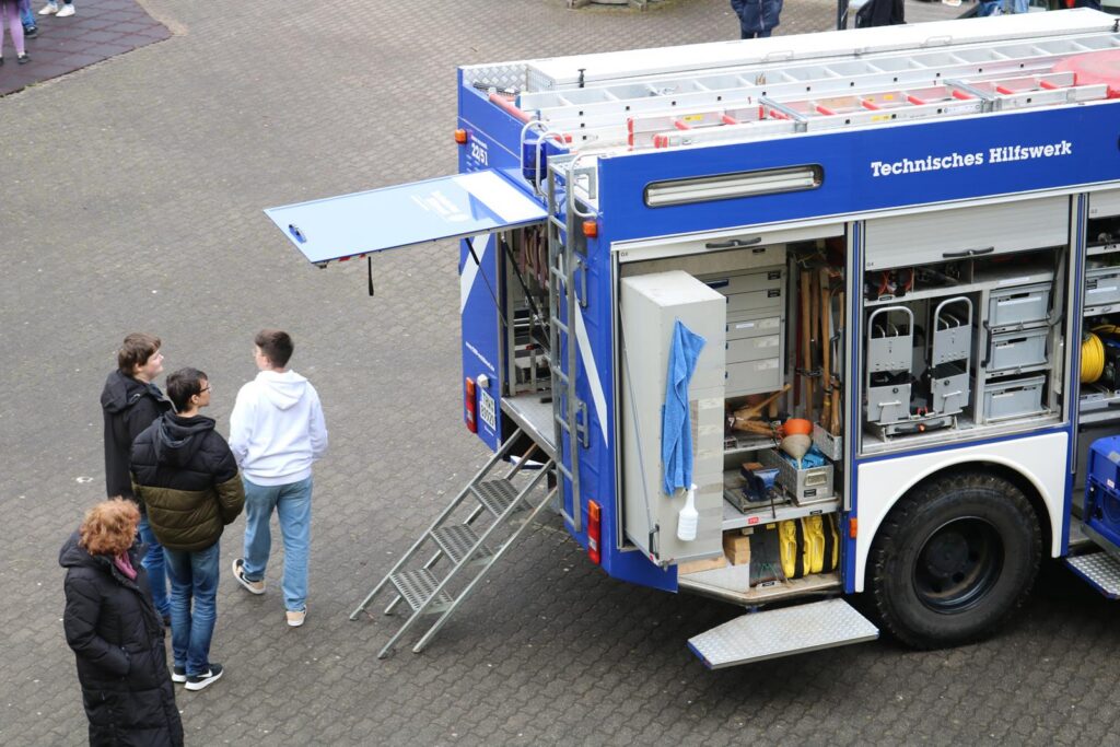 Technisches Hilfswerk Fahrzeug mit geöffnetem Heck und neugierigen Personen davor.
