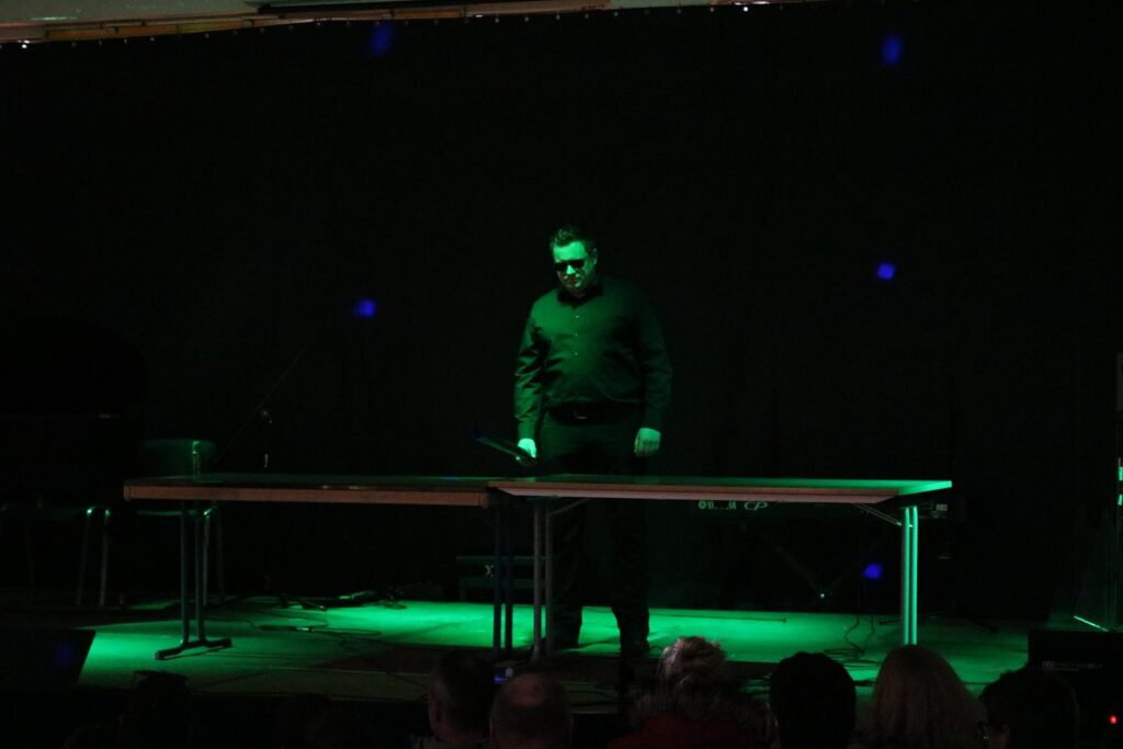 Mann steht an einem Tisch auf einer Bühne mit grünem Licht.