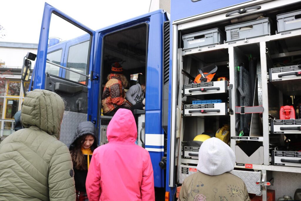 Gruppe von Kindern steht vor einem Fahrzeug mit geöffneten Türen und Ausrüstung.