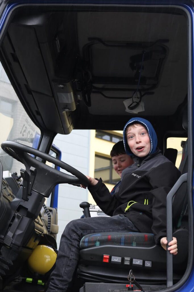 Zwei Kinder sitzen im Fahrersitz eines Traktors und schauen neugierig.