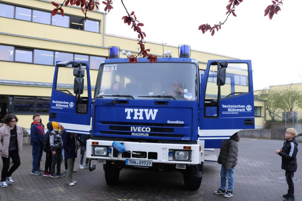 THW-Fahrzeug mit geöffneten Türen, Kinder stehen neugierig darum.