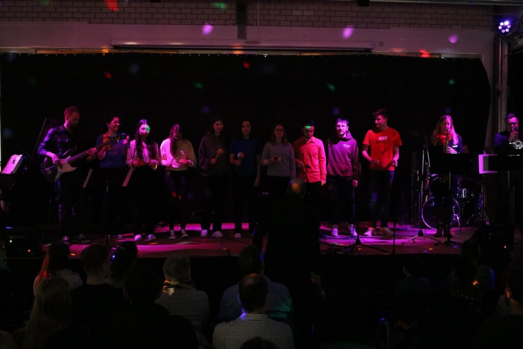 Schüler stehen auf der Bühne und singen in einer festlichen Atmosphäre.