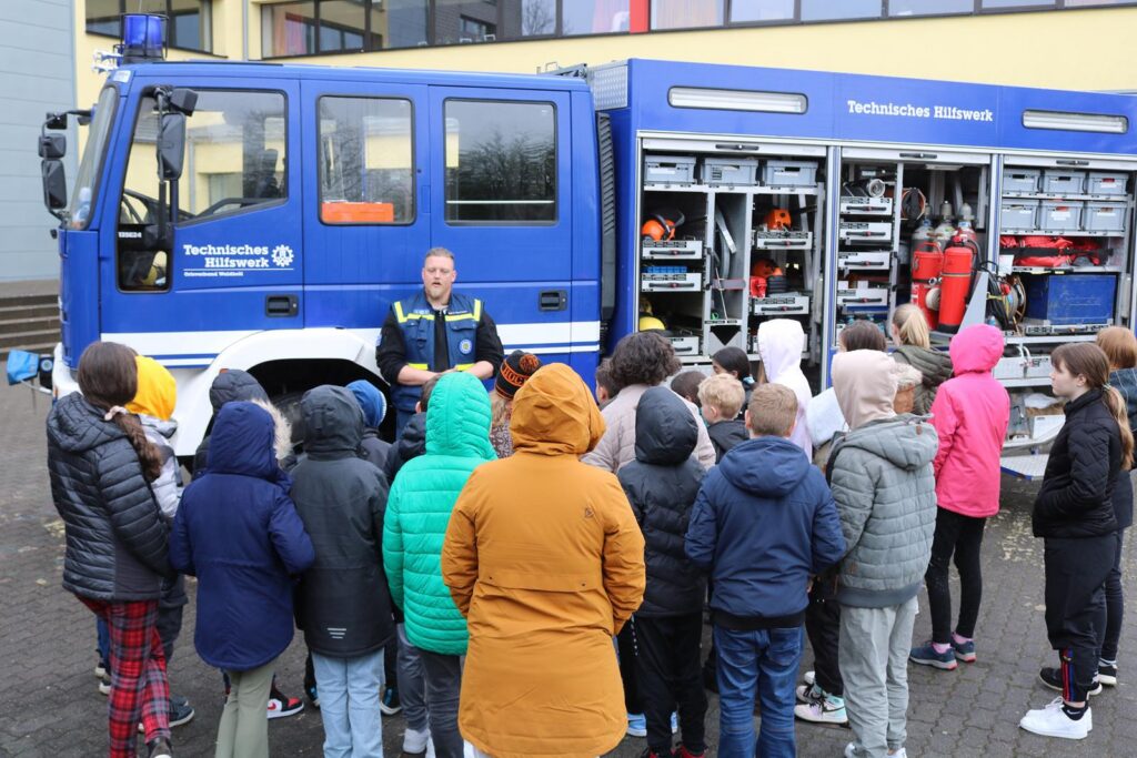 Gruppe von Kindern hört einem Feuerwehrmann neben einem Feuerwehrfahrzeug zu.