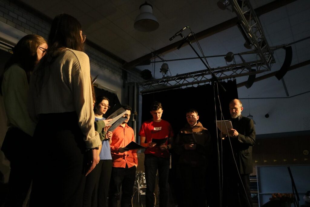 Gruppe von Personen steht auf der Bühne und singt in ein Mikrofon.