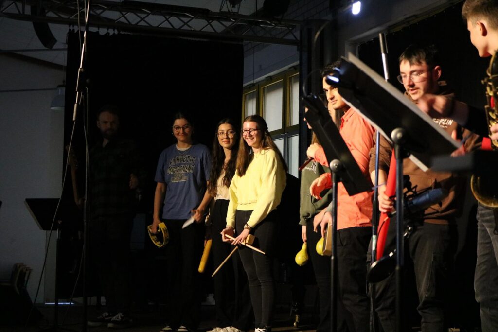 Musikgruppe mit Instrumenten auf der Bühne, alle stehen nebeneinander.