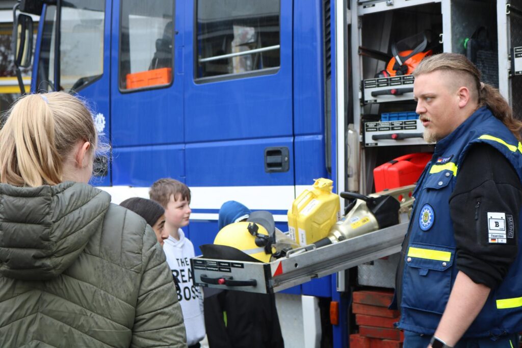 Ein Lehrer erklärt Schülern den Einsatz eines Feuerwehrfahrzeugs.