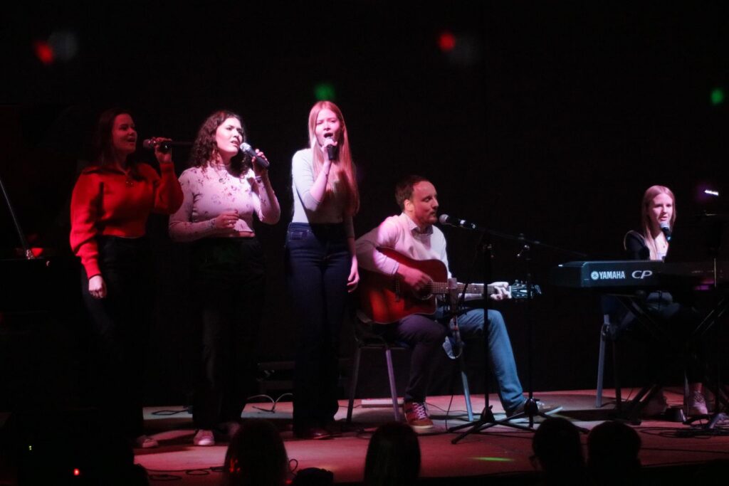 Eine Gruppe von fünf Personen singt und spielt Musik auf einer Bühne.