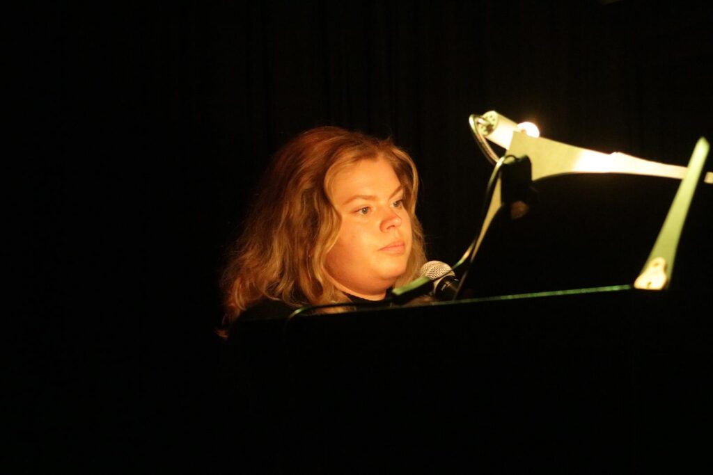 Schülerin spielt Klavier und singt bei einer Aufführung.