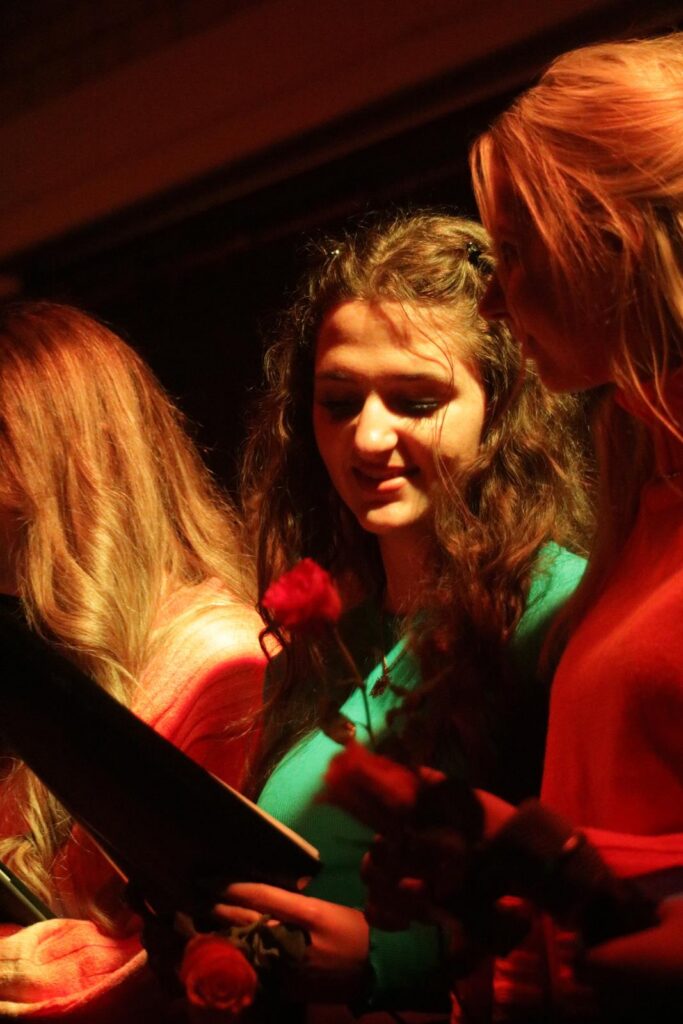 Drei Frauen bei einer Aufführung mit Rosen in der Hand. Rotes Lichtschein.