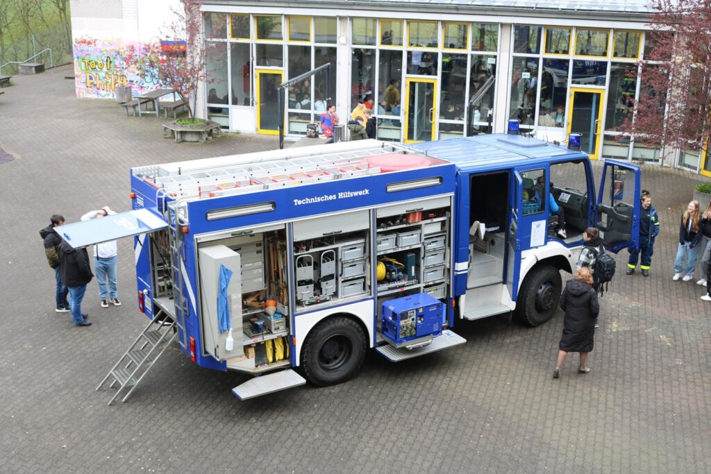 Feuerwehrfahrzeug mit geöffneten Türen, mehrere Personen stehen daneben.