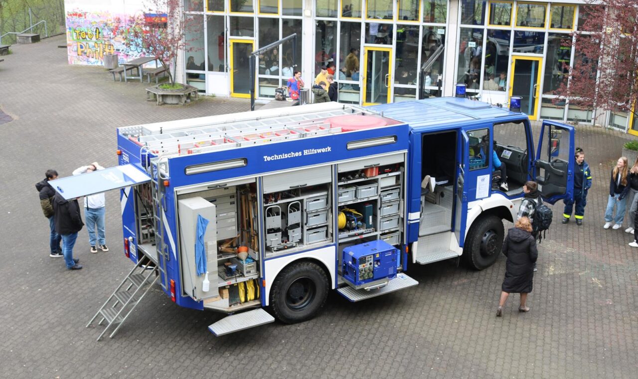 Feuerwehrfahrzeug mit geöffneten Türen, mehrere Personen stehen daneben.
