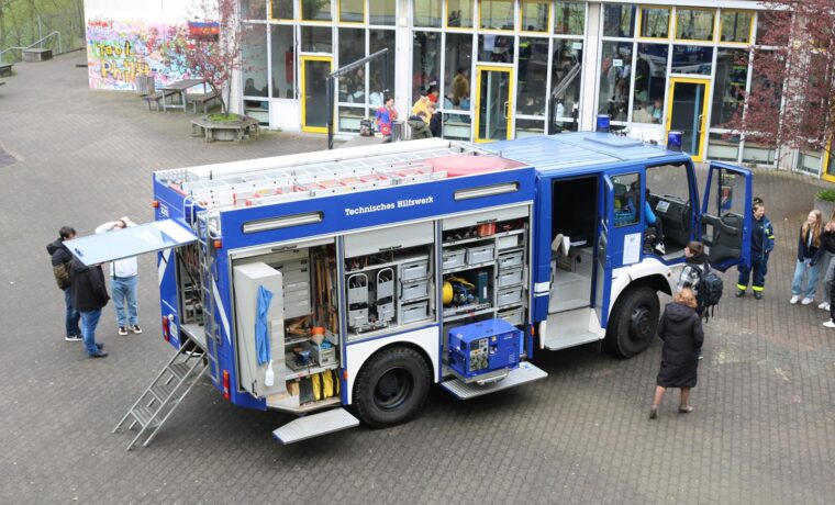 Feuerwehrfahrzeug mit geöffneten Türen, mehrere Personen stehen daneben.