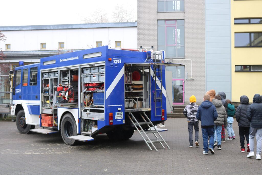 Rettungswagen steht auf dem Schulhof, Schüler betrachten ihn neugierig.