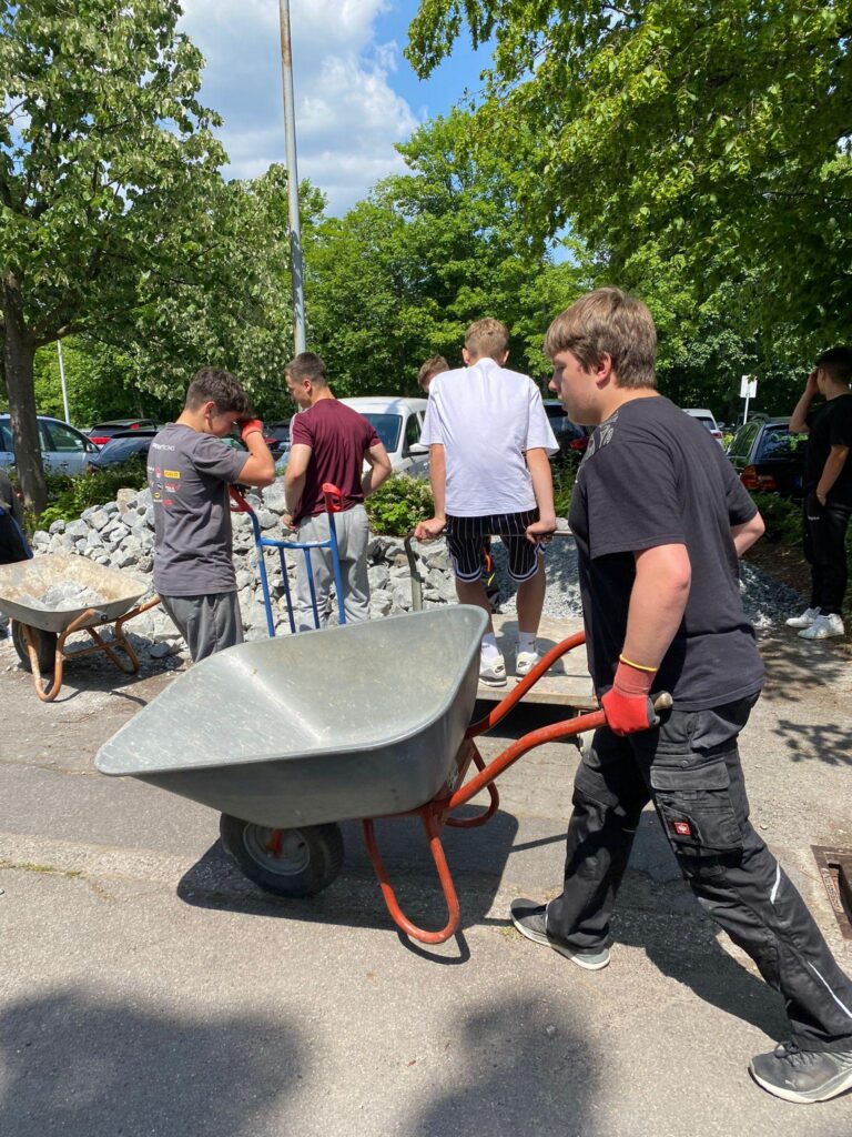 Schüler transportieren eine Schubkarre und arbeiten auf dem Schulgelände.