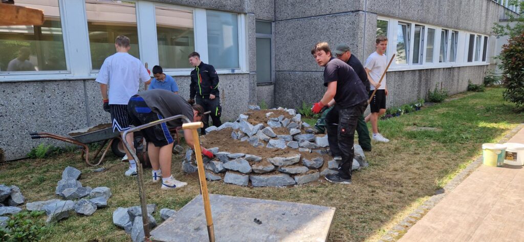 Schüler arbeiten im Freien an einem Landschaftsprojekt mit Steinen.