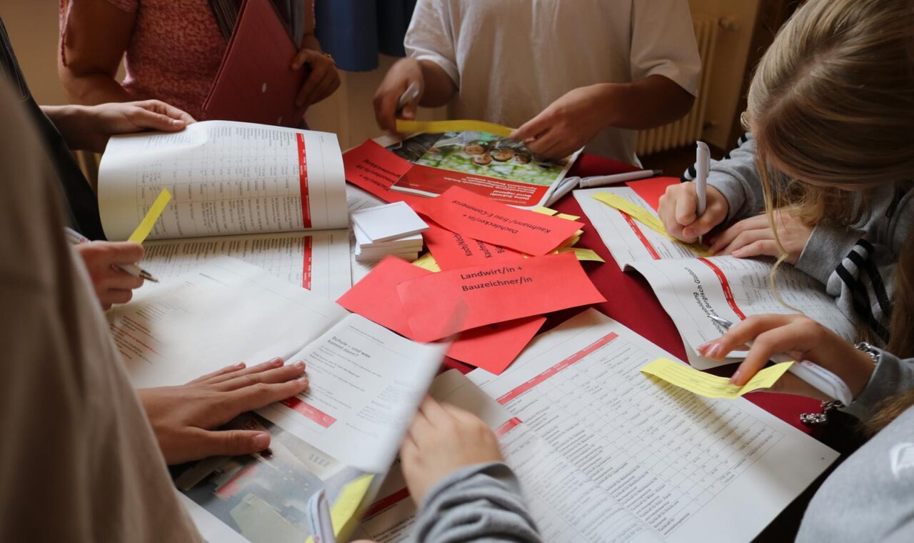 Schüler arbeiten an einem Tisch mit Heften und Notizen.