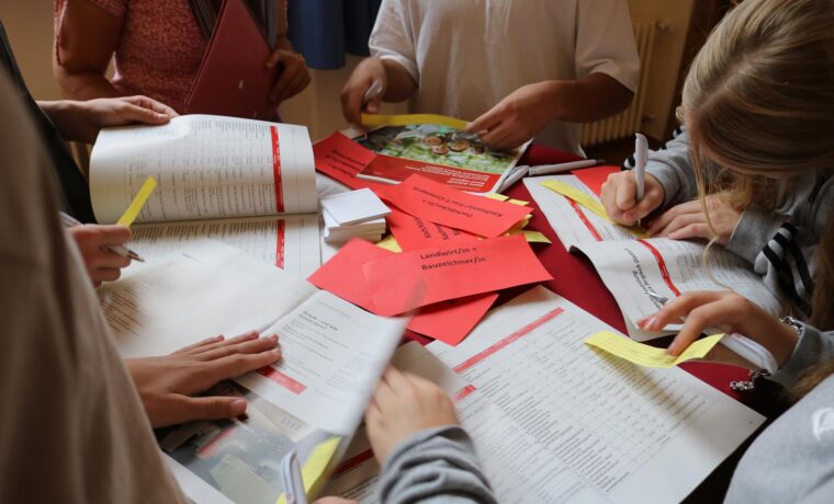 Schüler arbeiten an einem Tisch mit Heften und Notizen.