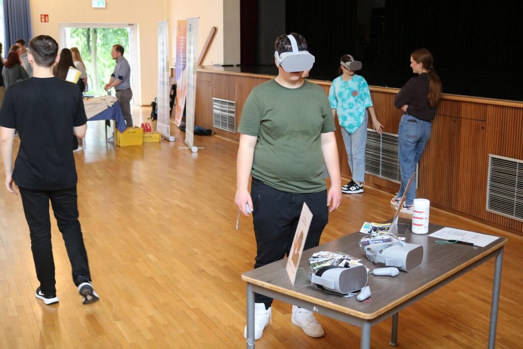 Schüler mit VR-Brille steht an einem Tisch mit technischen Geräten.