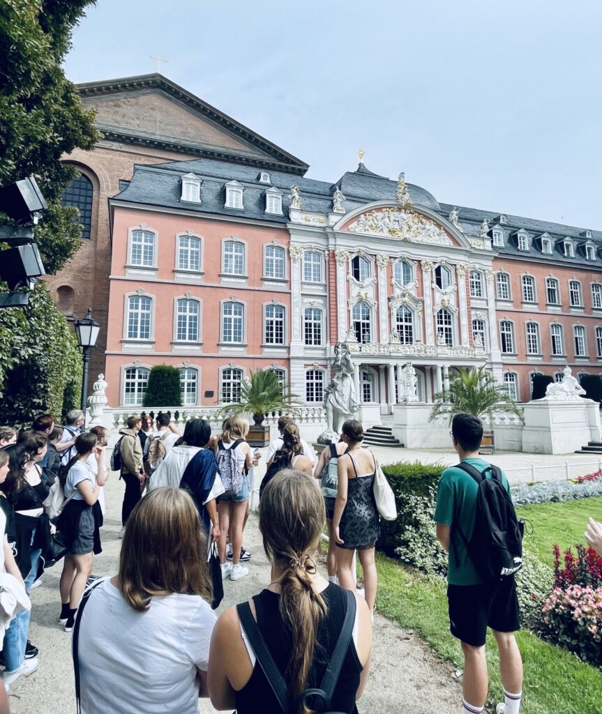 Gruppe von Schülern steht vor einem historischen Gebäude mit grünen Anlagen.
