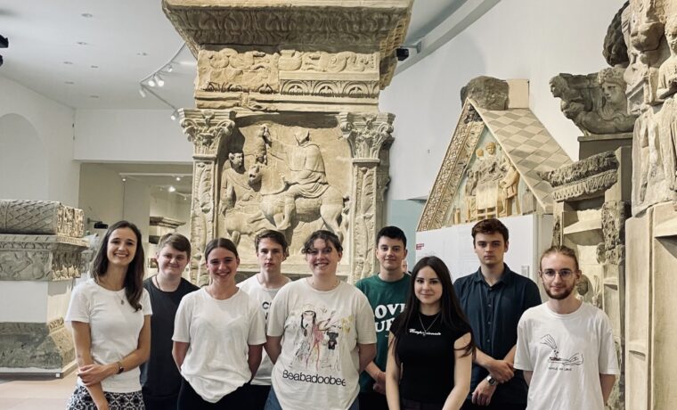 Gruppe von Schülern steht in einem Museum vor einer steinernen Säule.