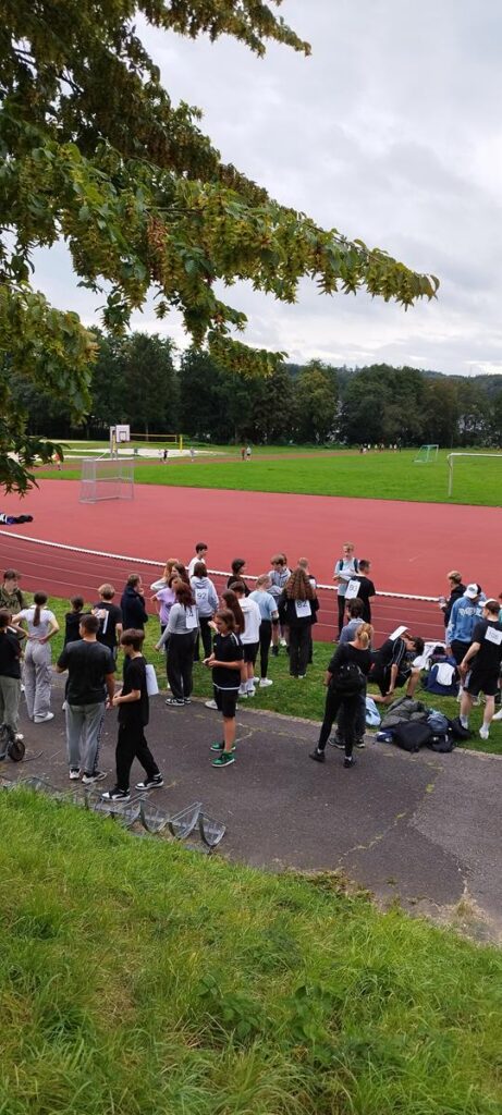 Gruppenschüler auf einem Sportplatz mit Laufbahn und Rasenfläche.