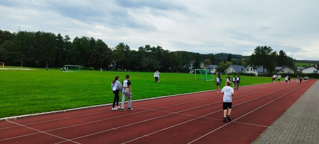 Schüler auf einem Sportplatz mit Laufbahn und Fußballtoren.