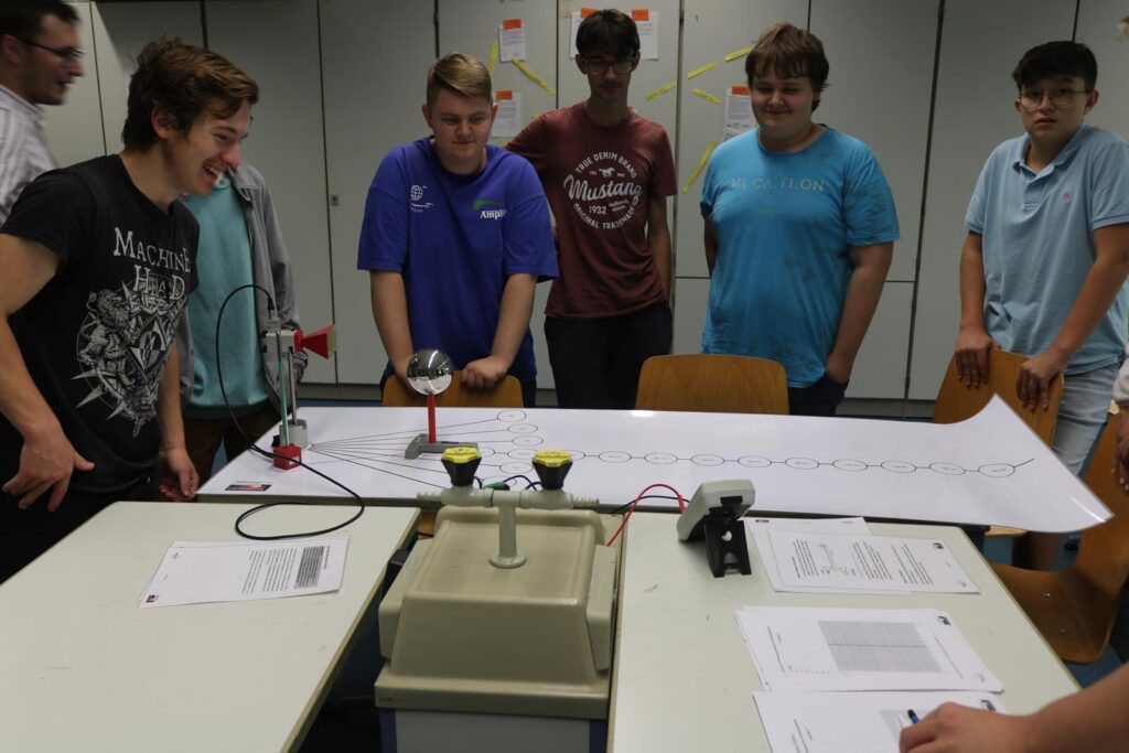 Schüler beobachten Experimente an einem Tisch mit Geräten und Dokumenten.