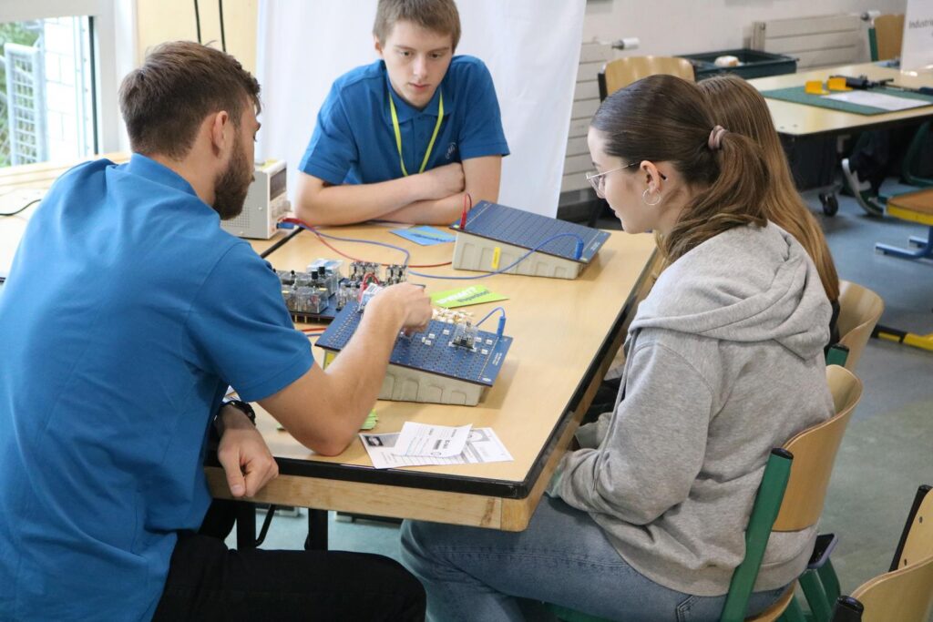 Gruppe von Schülern arbeitet an einem Tisch mit Elektronikbaukästen.