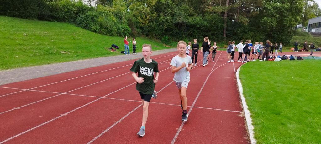 Schülerinnen laufen auf einer Sportbahn, im Hintergrund sind weitere Schüler.