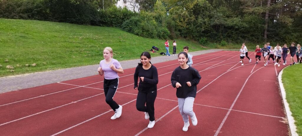 Schülerinnen und Schüler laufen auf einer Laufbahn. Grünflächen im Hintergrund.