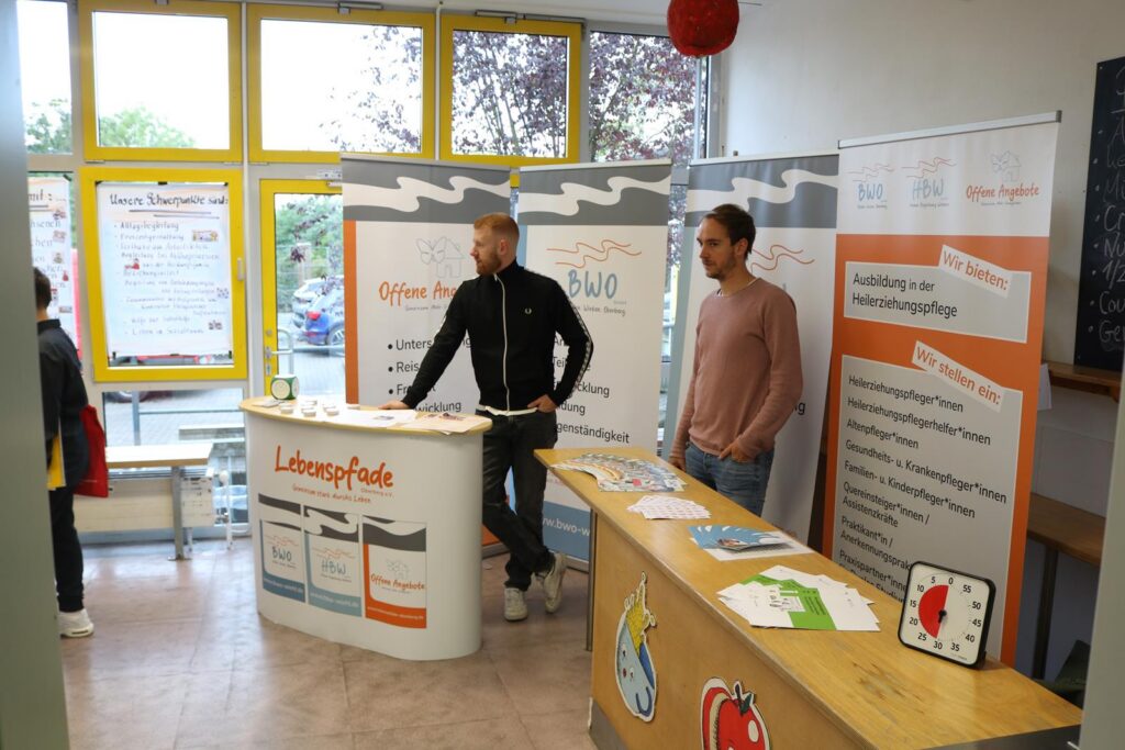 Messestand mit zwei Personen und Informationsmaterialien in einem hellen Raum.
