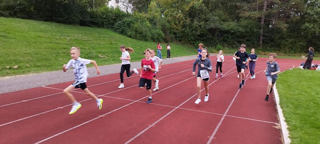 Kinder laufen auf einer roten Laufbahn während eines Sportevents.