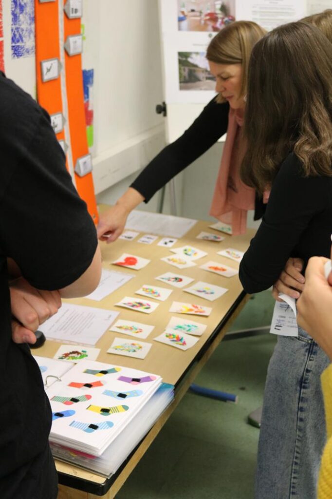 Lehrerin zeigt Karten auf einem Tisch, Schülerinnen und Schüler beobachten.